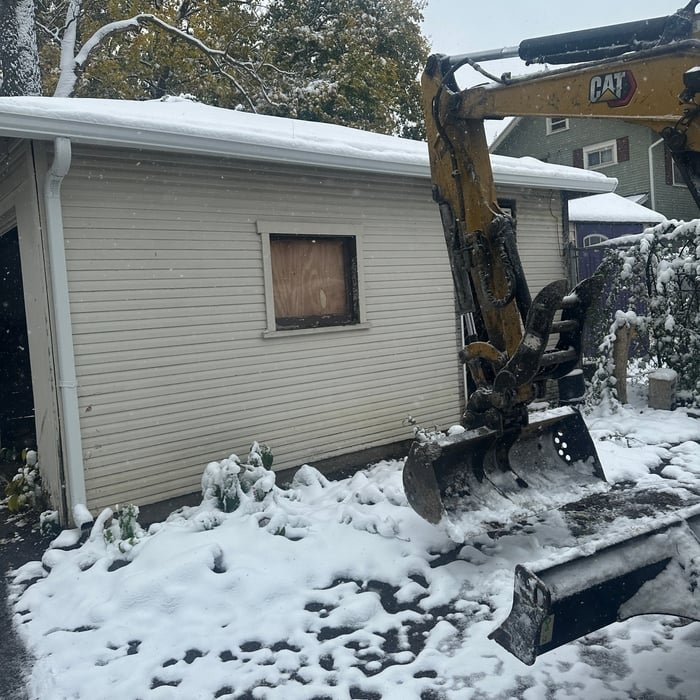CAT excavator positioned beside a garage for demolition
