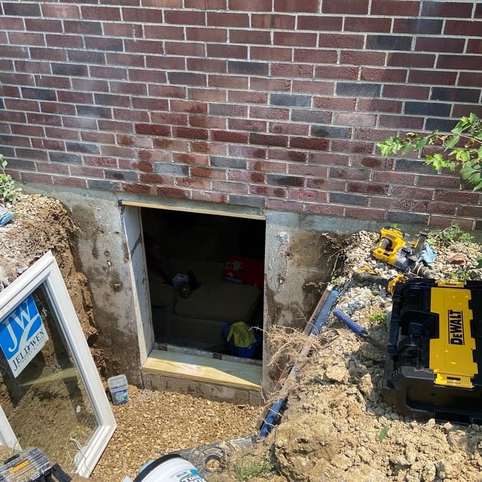 Basement egress window opening excavated beside a brick home